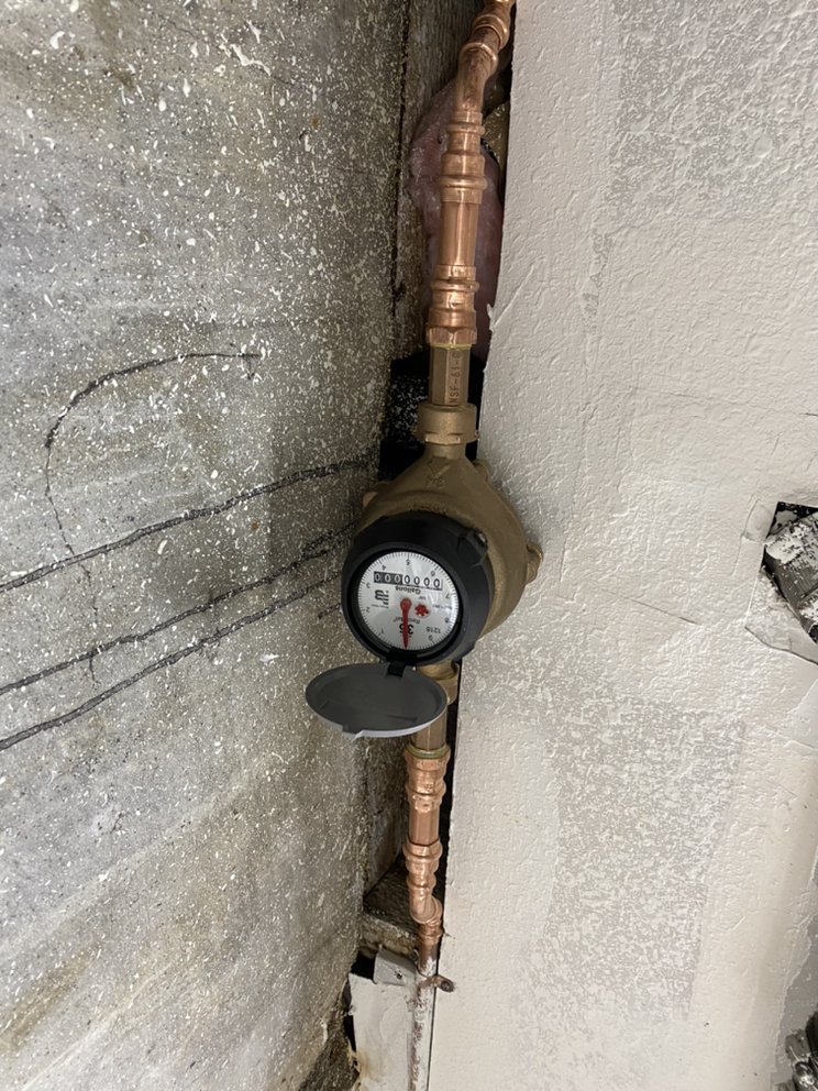 Newly installed water meter and copper piping against a home's foundation